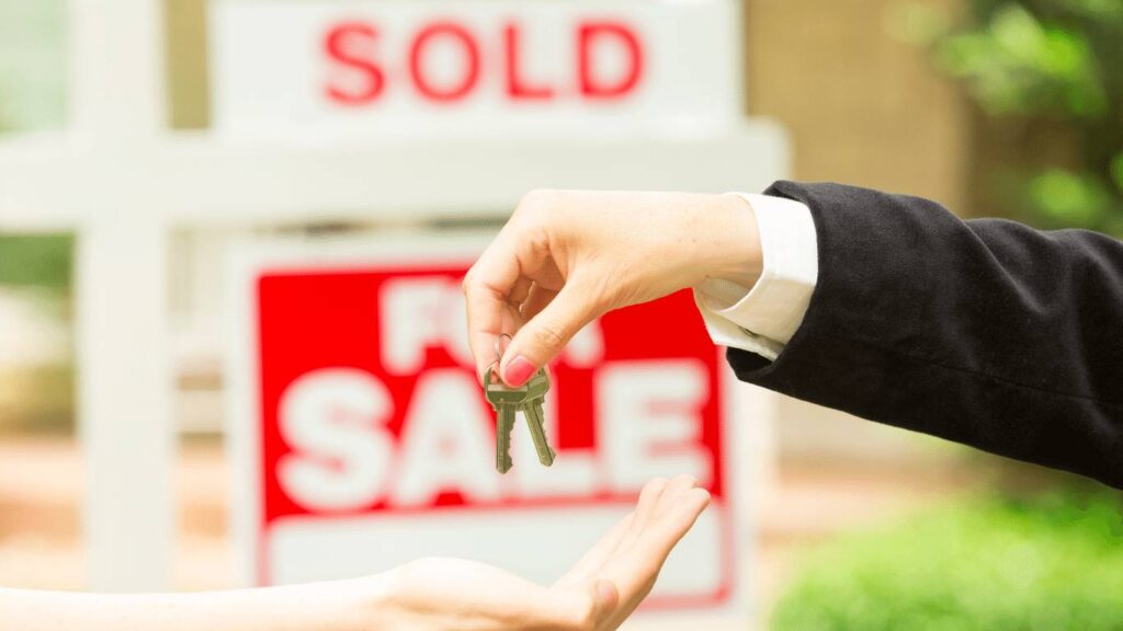 Real estate agent handing over house keys to a new homeowner in front of a sold property.